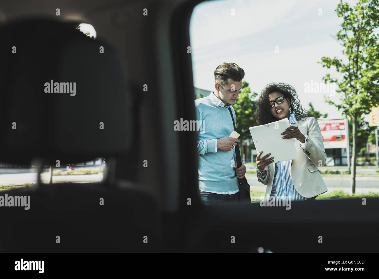 Young man and woman discussing document outside car Stock Photo - Alamy