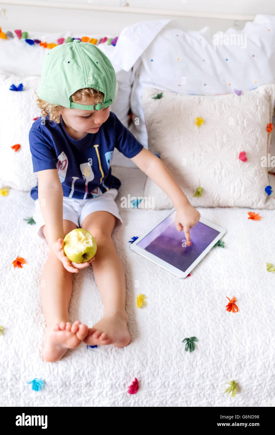 Little boy sitting on the couch with an apple using digital tablet Stock Photo
