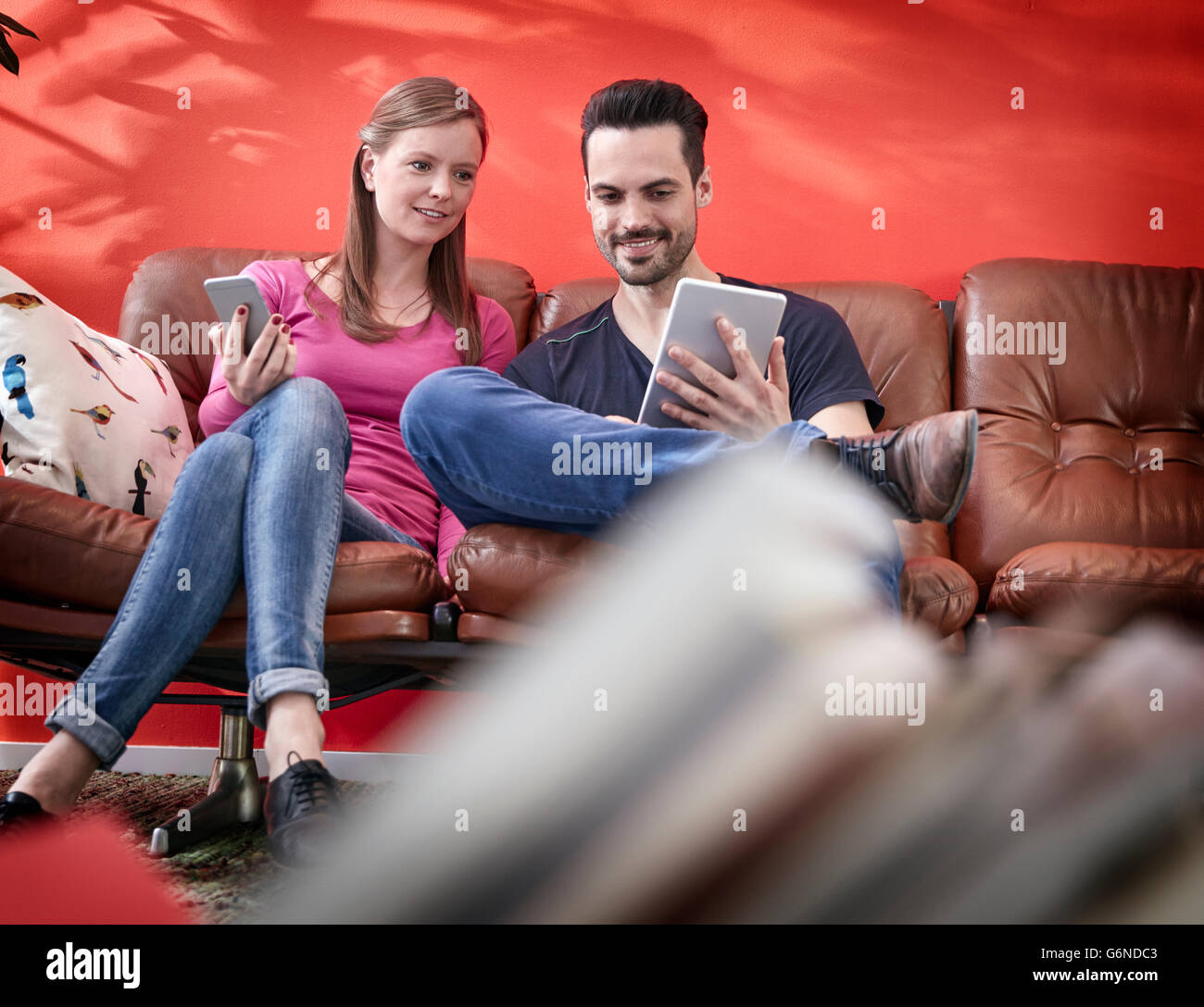 Young businessman and woman sitting on vintage couch using digital gadgets Stock Photo