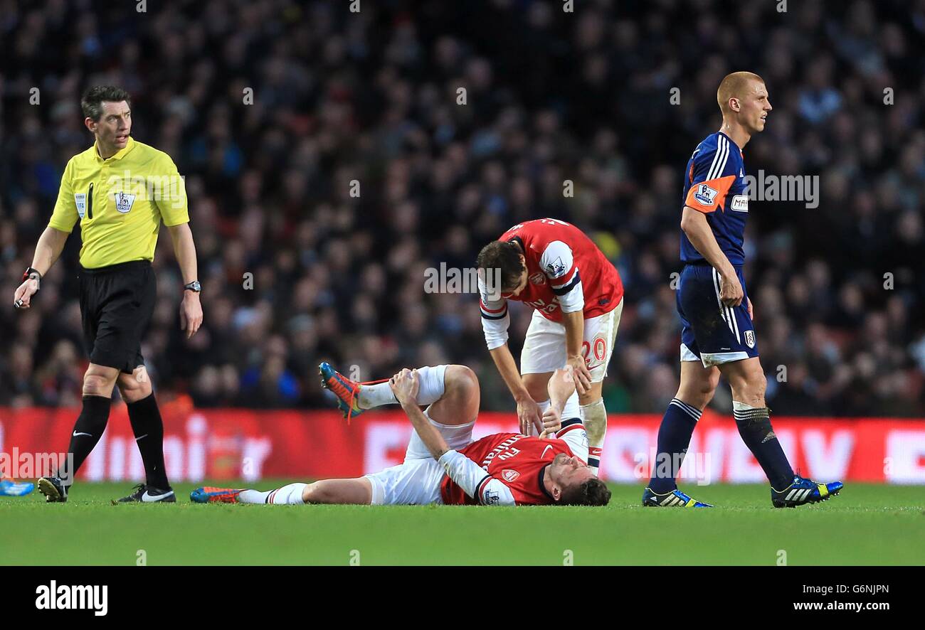 Arsenal's Olivier Giroud lies on the ground injured as team-mate Mathieu Flamini checks on his condition Stock Photo