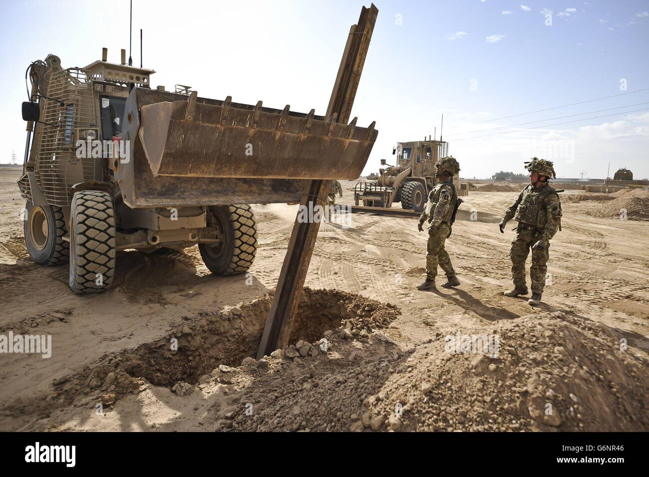 Soldiers watch as n Army digger places a huge metal post in a hole where British Royal Engineers are fixing a new road sign to replace previous signs that have been stolen by children. Stock Photo