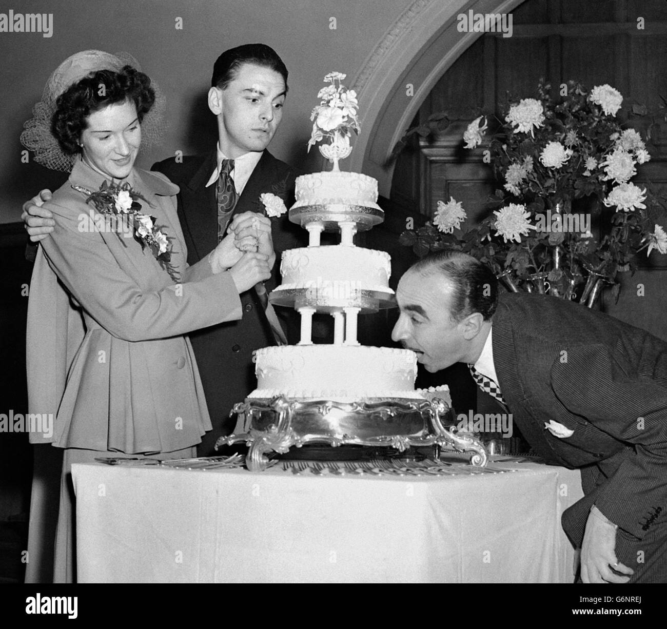 Radio comedian Bob Monkhouse and his bride Elizabeth Thompson, a former nurse from Belfast at their wedding reception at Caxton Hall, London. Harold Berens is taking a bite of their cake as they attempt to cut it. Stock Photo