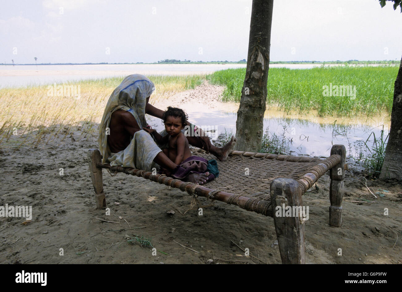India Bihar , submergence at Bagmati river a branch of ganges due to heavy monsoon rains and melting Himalaya glaciers, mother with child on charpoy, traditional bed, destroyed paddy fields Stock Photo
