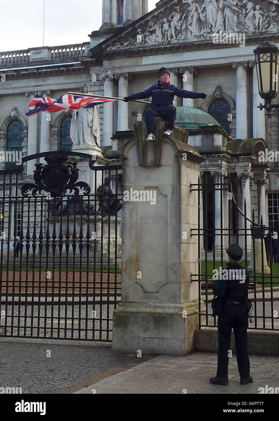 Flag protestor. A lone Union flag protestor, waving a Union flag, sits on the gates outside City Hall, Belfast. Stock Photo