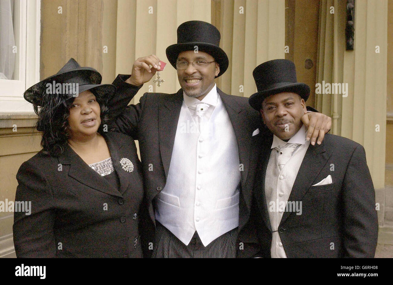 Former Boxer Michael Watson, who was brain damaged in a fight with Chris Eubank 13 years ago, proudly displays his MBE, as he stands with his mother Joan and brother Jeffrey, after receiving the honour from Britain's Queen Elizabeth II at an Investiture Ceremony at Buckingham Palace, London. Mr Watson, 38, who doctors said would never walk again, stepped up unaided to receive the MBE in recognition of his work for disabled sport. Stock Photo