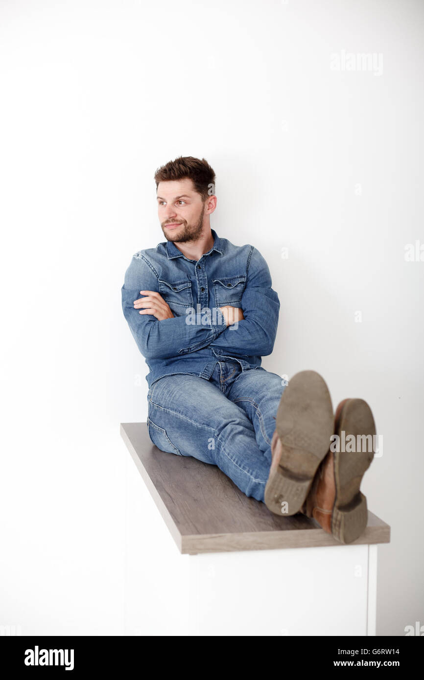 Portrait of a confident man in a denim shirt. A man sits on a wooden board. Stock Photo