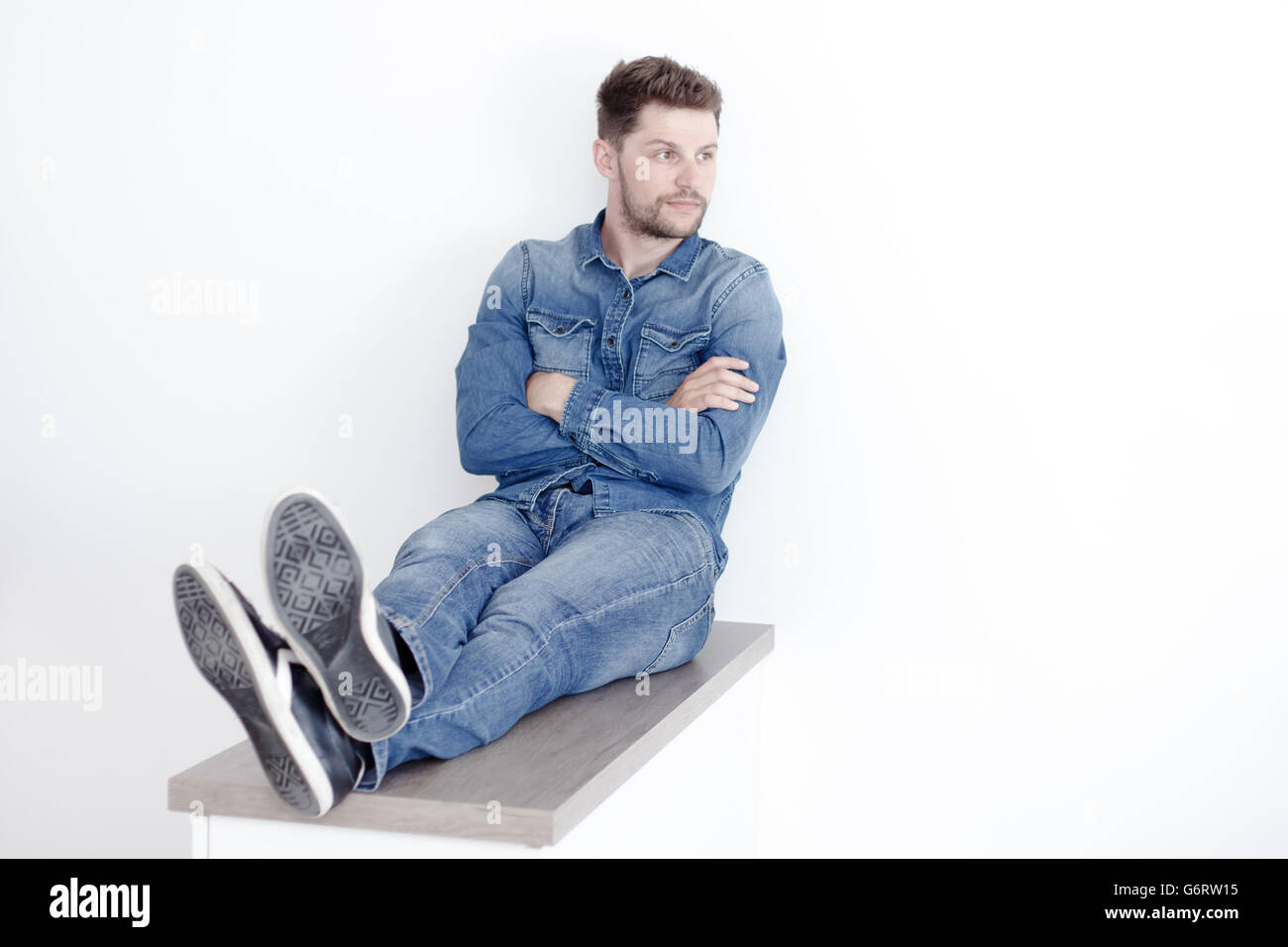 Portrait of a confident man in a denim shirt. A man sits on a wooden board. Stock Photo