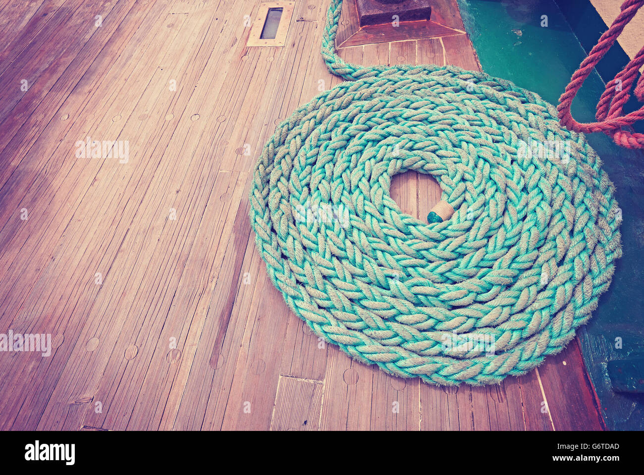Vintage toned wide angle picture of mooring rope on wooden deck of a sailboat. Stock Photo