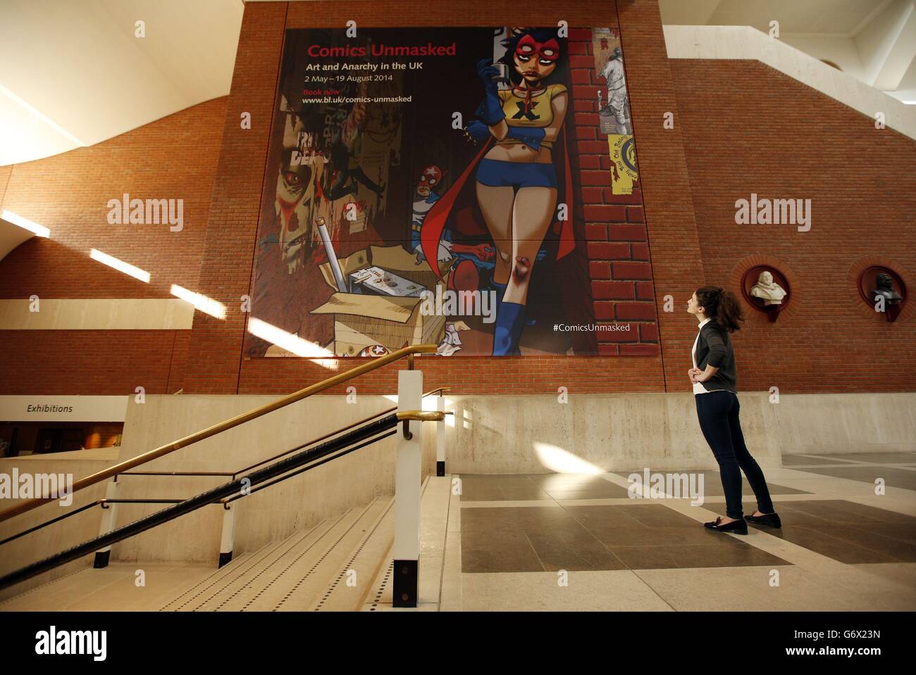 A British Library staff member walks past the tapestry style poster of artwork by Gorillaz co-creator Jamie Hewlett, that was commissioned for the upcoming exhibition 'The Comics Unmasked: Art and Anarchy in the UK' at The British Library, central London. Stock Photo