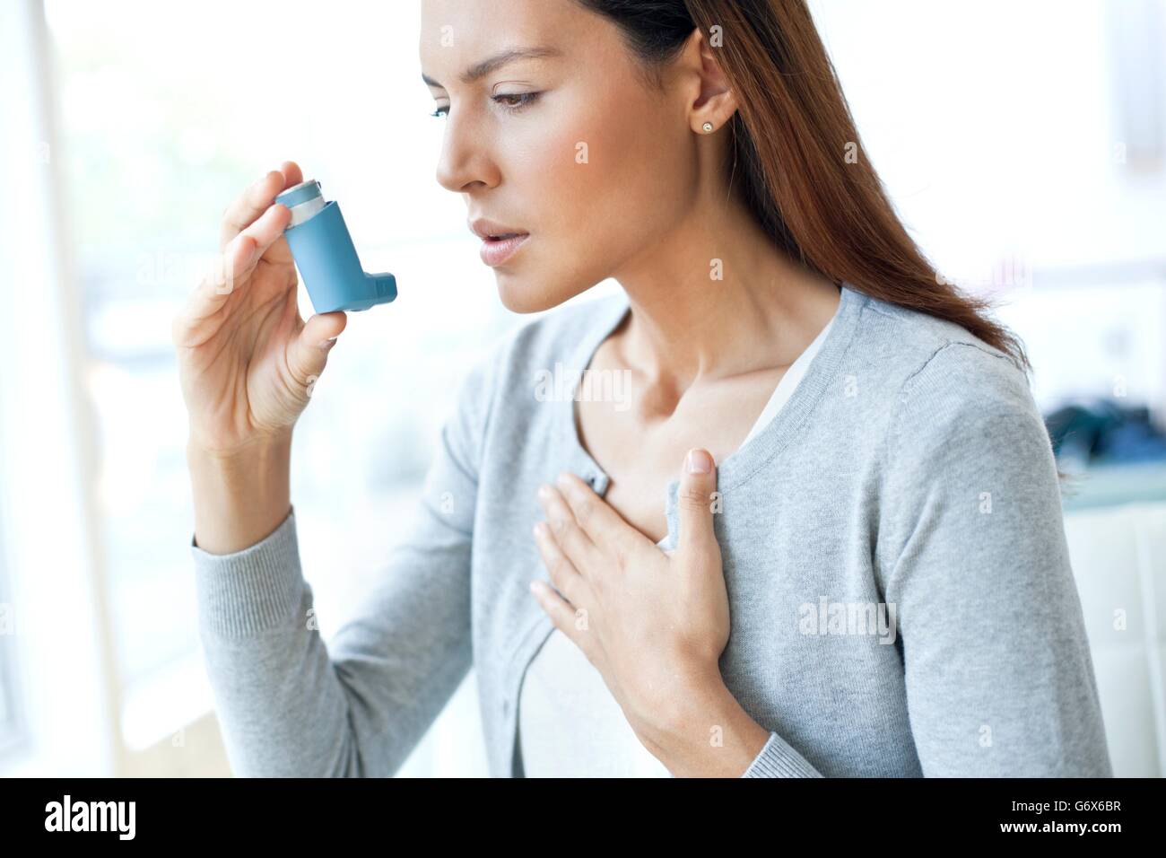 MODEL RELEASED. Young woman using an inhaler and touching her chest. Stock Photo