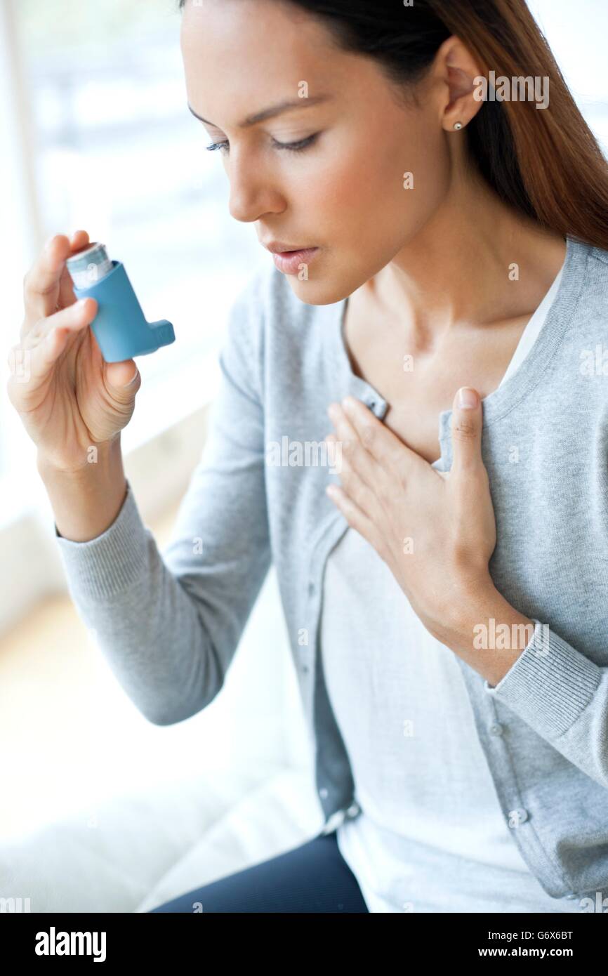 MODEL RELEASED. Young woman using an inhaler and touching her chest. Stock Photo