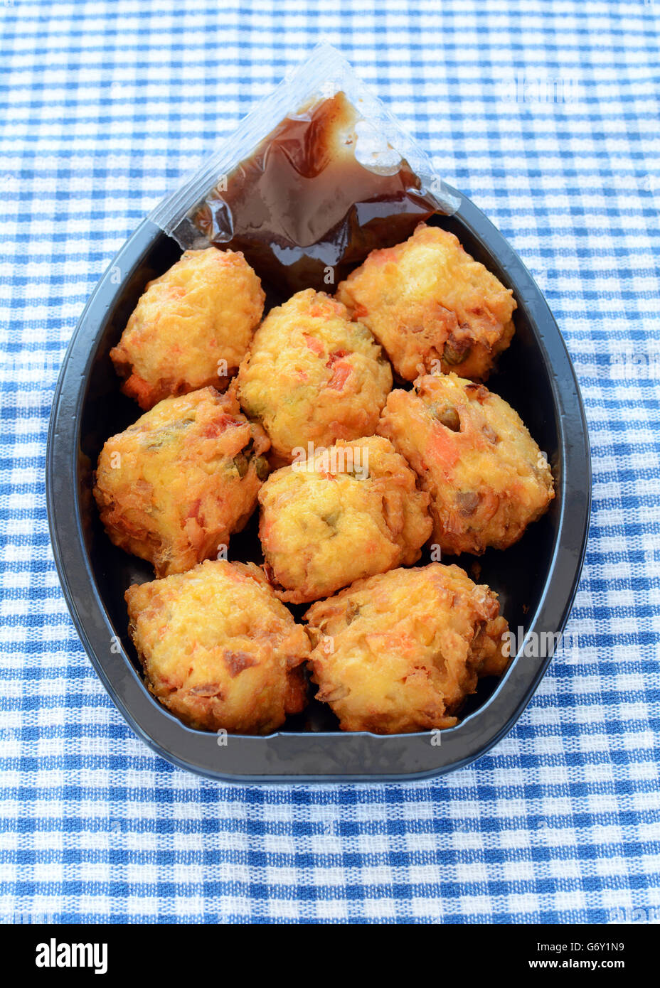 Fresh vegetable pakoras with tamarind chutney prepared by the delicatessan in plastic container on blue and white check cloth in Stock Photo