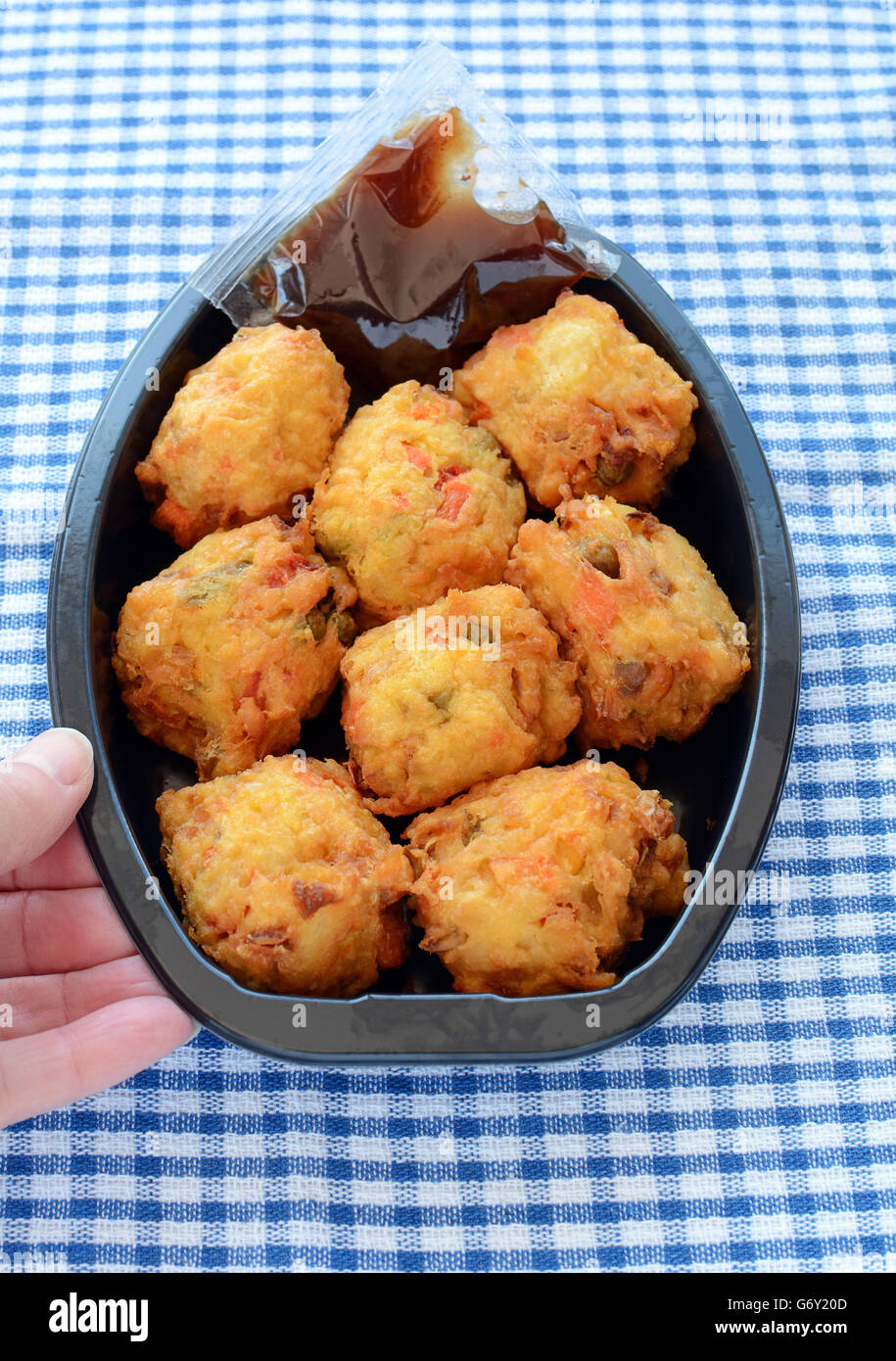 Fresh vegetable pakoras with tamarind chutney prepared by the delicatessan in plastic container on blue and white check cloth in Stock Photo