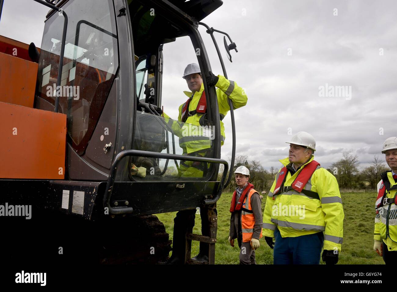 Prime Minister David Cameron climbs up to the cab of an excavator as he is shown the dredging operation on site at the River Parrett, near Burrowbridge, Somerset, where repair and recovery from the floods earlier in 2014 are taking place. Stock Photo