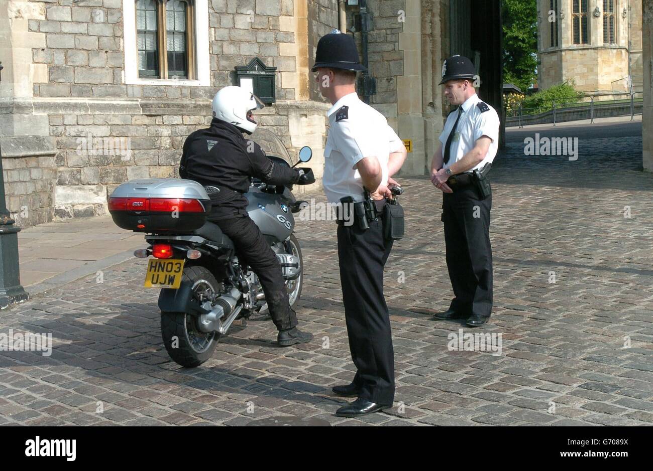 Police officers check a motorcyclist entering the Henry VIII gate at Windsor Castle. A man arrested at the castle on suspicion of impersonating a police officer was still being questioned along with his girlfriend at a London police station. The castle is frequently home to member of the Royal family. Stock Photo