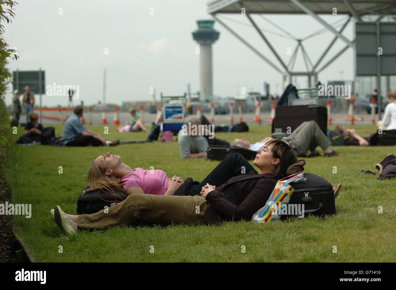 Bride-to-be Anna Spencer (left) and bridesmaid Eryl Baum rest in the sunshine outside Stansted airport, near Bishop's Stortford, after an air traffic computer breakdown, caused a four-hour delay to their flight to Edinburgh. The privatised National Air Traffic Services, (Nats), the firm that operates air traffic control in the UK, said passenger safety was never put at risk despite the computer crash and that they believed they had located the problem, at an operations centre in West Drayton, near Heathrow. Stock Photo