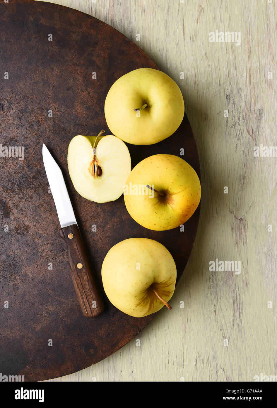 Golden Delicious apple still life with knife. Dark round surface on rustic table. Stock Photo