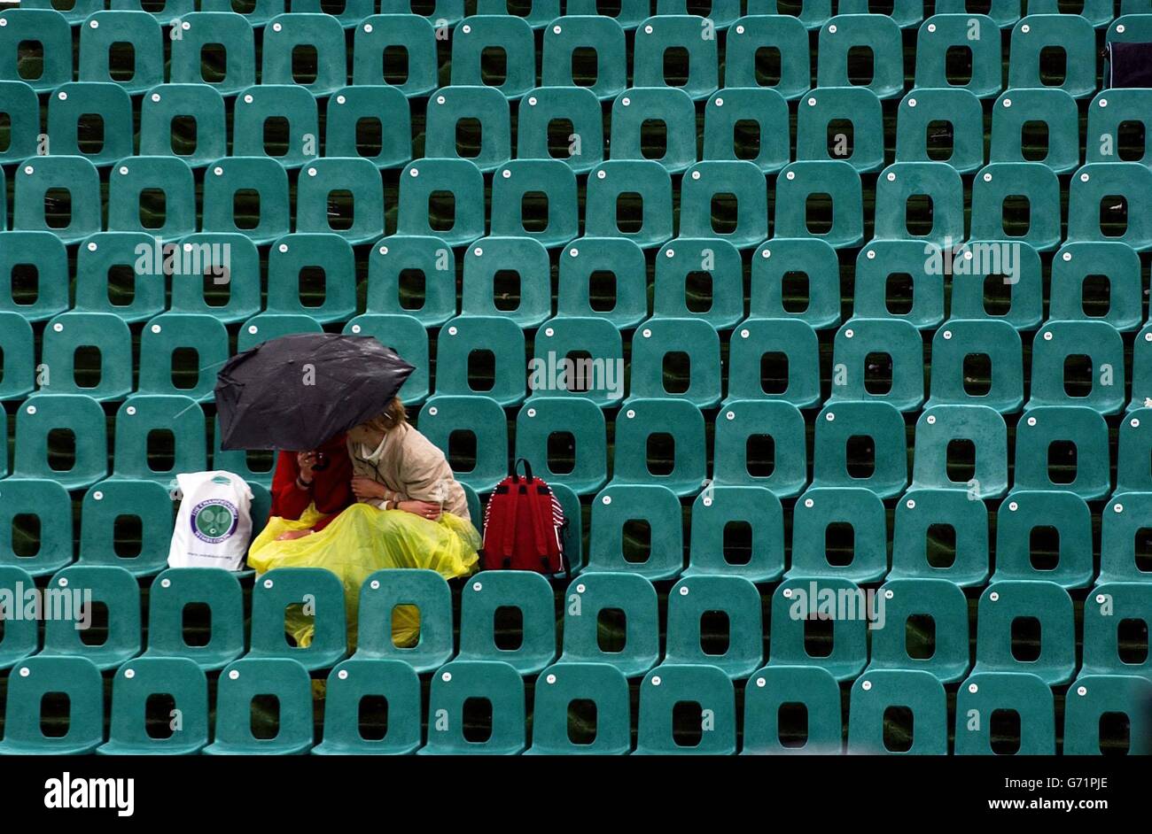 Tennis fans take cover under umbrellas at The Lawn Tennis Championships in Wimbledon, London, where rain and gales delayed the start of play. , NO MOBILE PHONE USE. Stock Photo