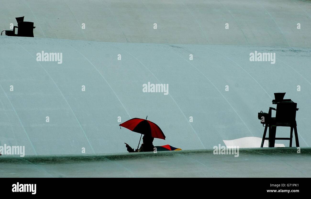 Tennis fans take cover under umbrellas at The Lawn Tennis Championships in Wimbledon, London, where rain and gales delayed the start of play. Stock Photo