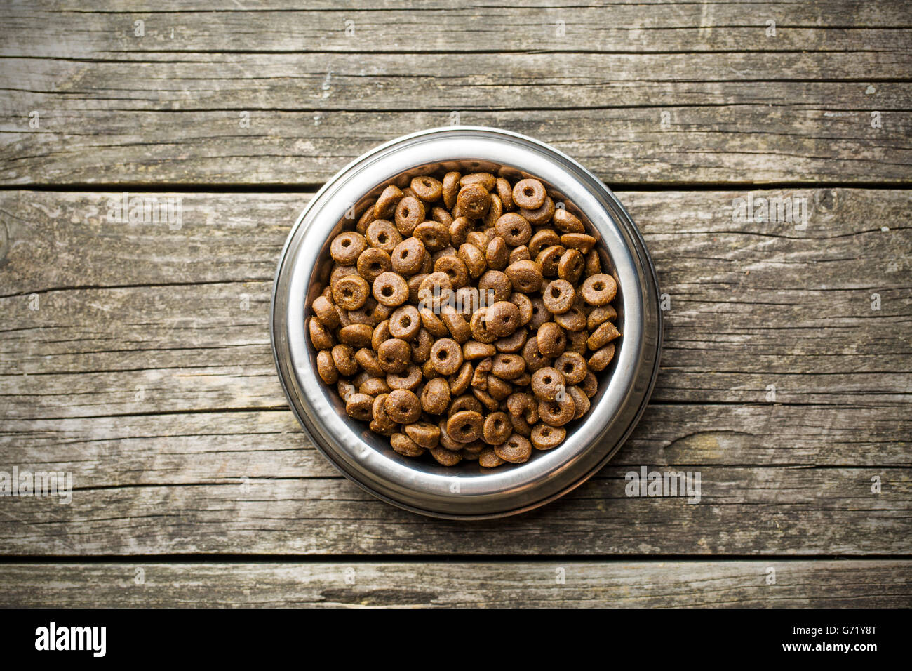 Dry kibble dog food in bowl on old wooden table. Top view. Stock Photo