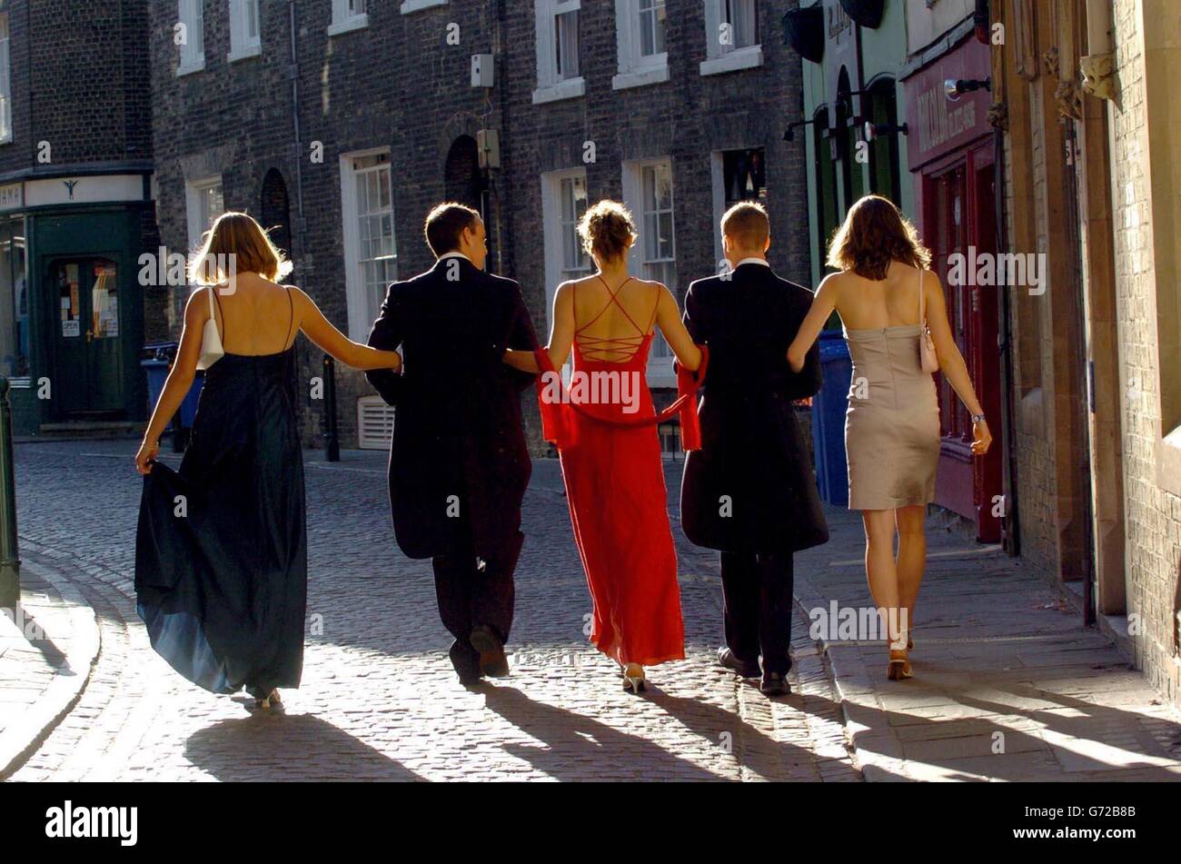 Cambridge University students make their way home through the early morning sunshine, after the end of term May Ball at Trinity College. The college balls, held during May Week - a fortnight in June - are the traditional way for students to let their hair down after taking their end of year exams. Stock Photo