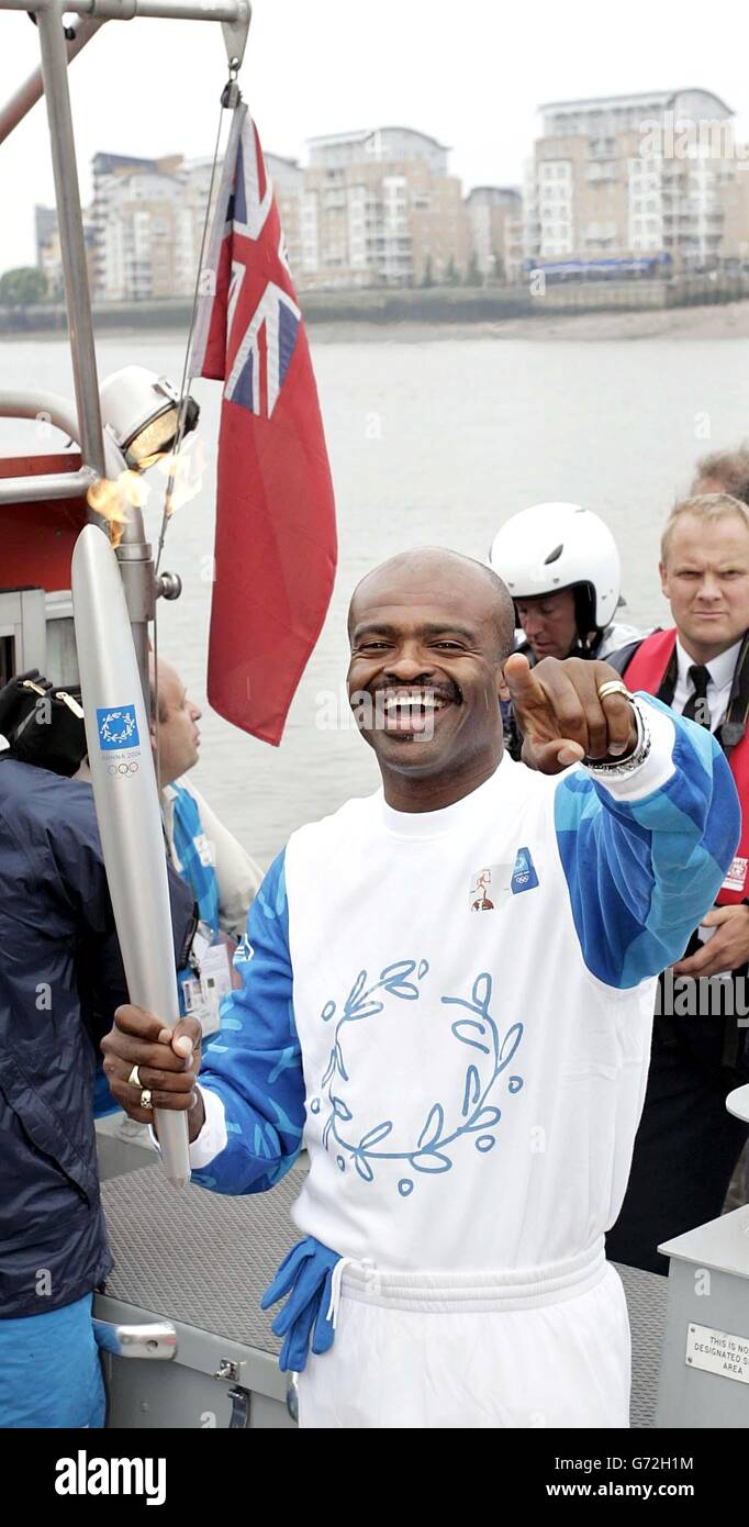 Former athlete Kriss Akabusi carries the torch across the River Thames from Cutty Sark Gardens, London, on the 23rd leg of the Olympic Torch Relay 2004. Stock Photo