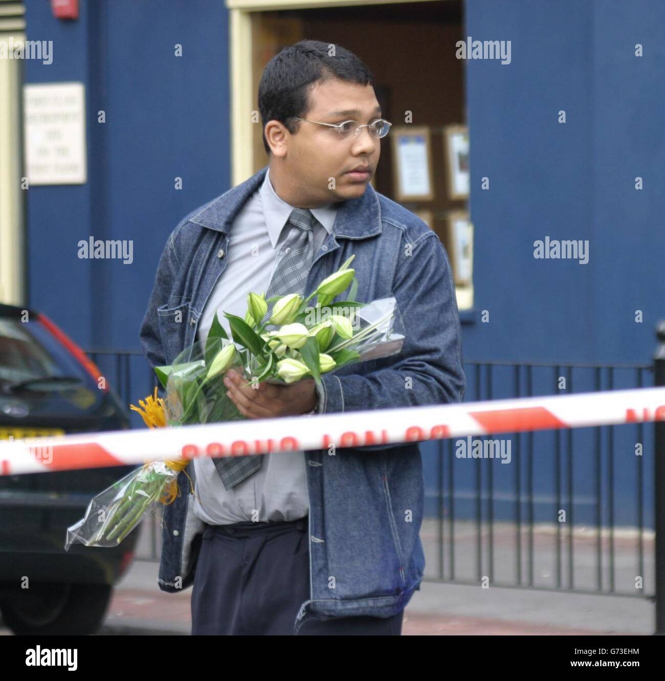 A man brings flowers to the scene in Bethnal Green, east London, where two firefighters died battling a blaze in a three-storey building. It is understood that the pair were on the top floor of the building, which had a shop on the ground floor and flats above, when it appeared that the floor beneath them gave way. They were seriously injured and rushed to hospital, where they both subsequently died. Stock Photo