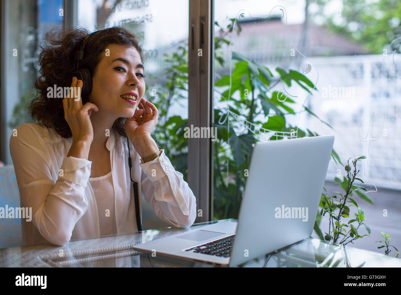 Asian girl sitting at a table in a cafe with a laptop, in headphones to enjoy music. Stock Photo