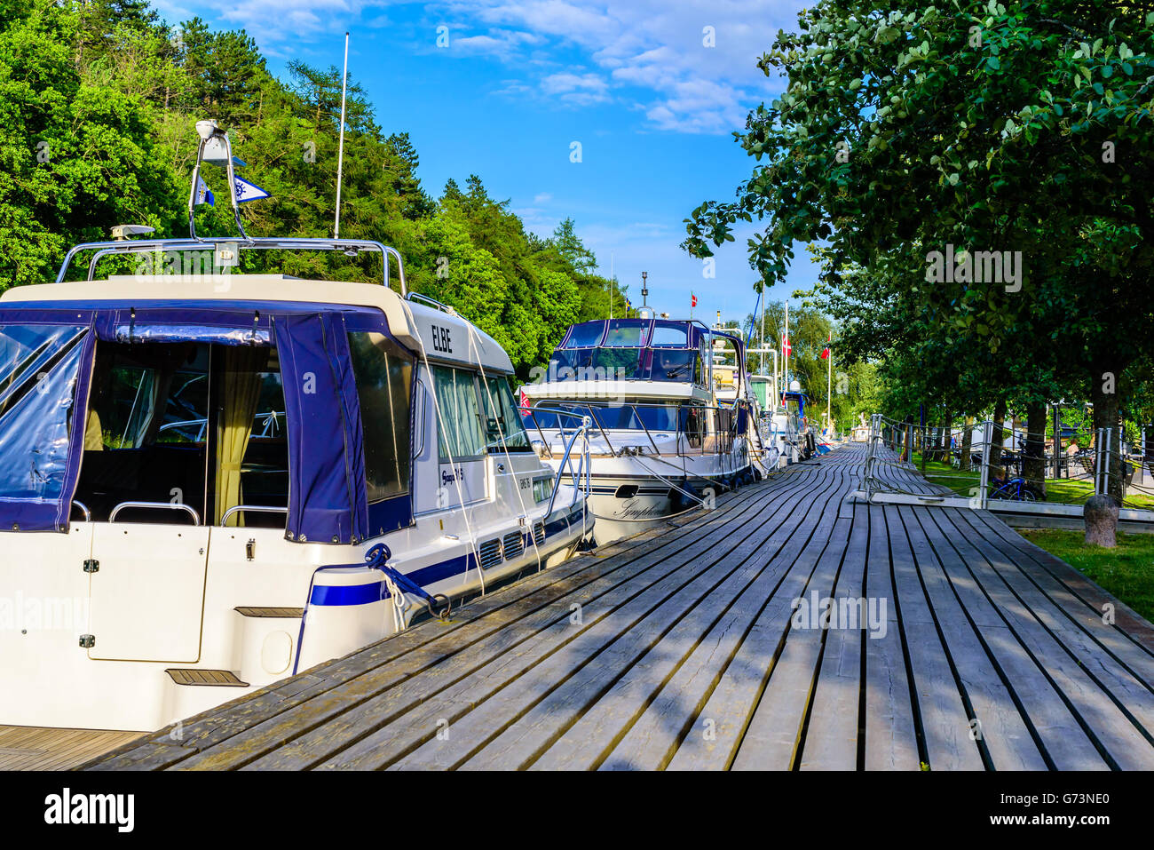Soderkoping, Sweden - June 19, 2016: Moored motorboats at a wooden pier along the Gota canal. First boat is a Saga 315 powerboat Stock Photo