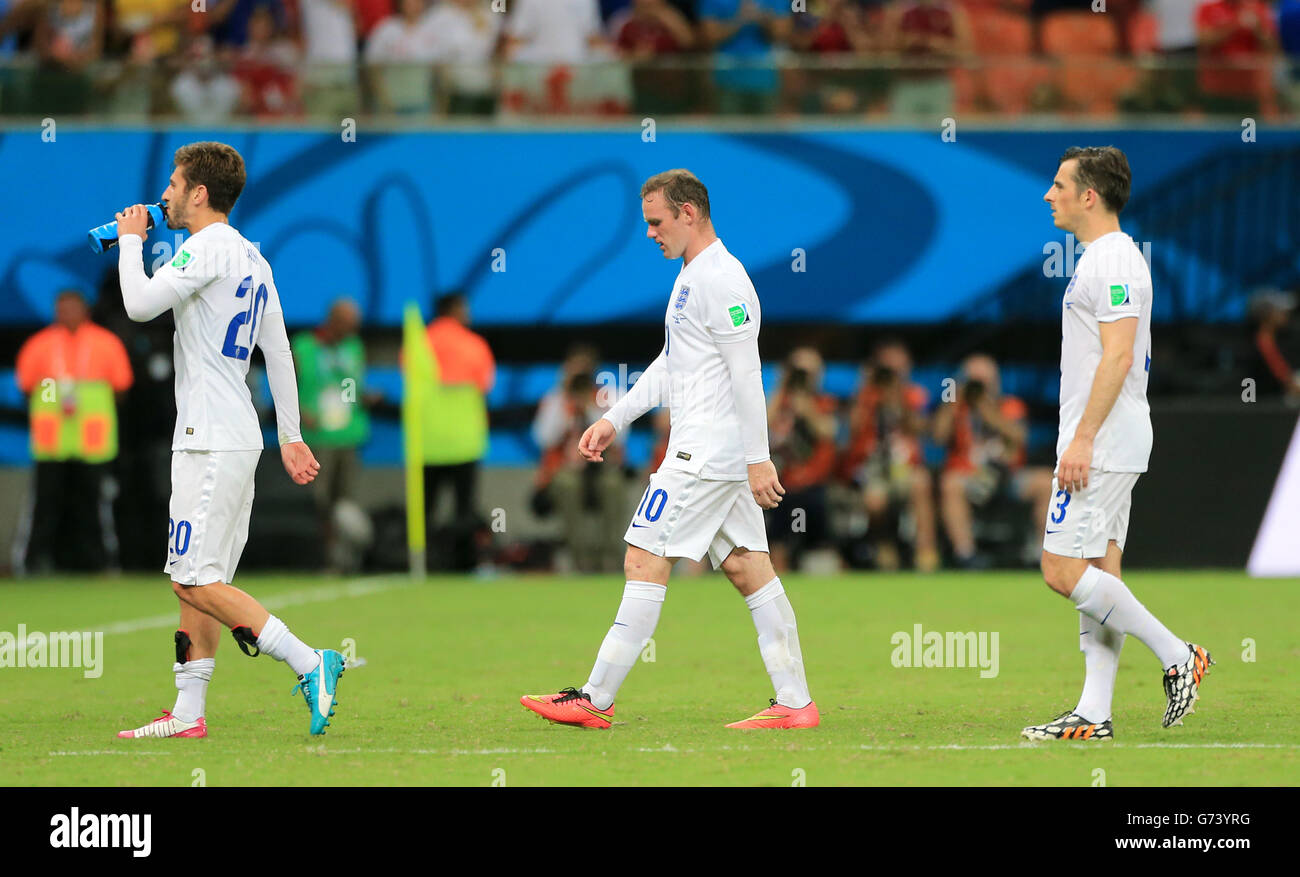 England's Wayne Rooney (centre), Adam Lallana (left) and Leighton Baines walk off the pitch dejected after the final whistle during the FIFA World Cup, Group D match at the Arena da Amazonia, Manaus, Brazil. Stock Photo