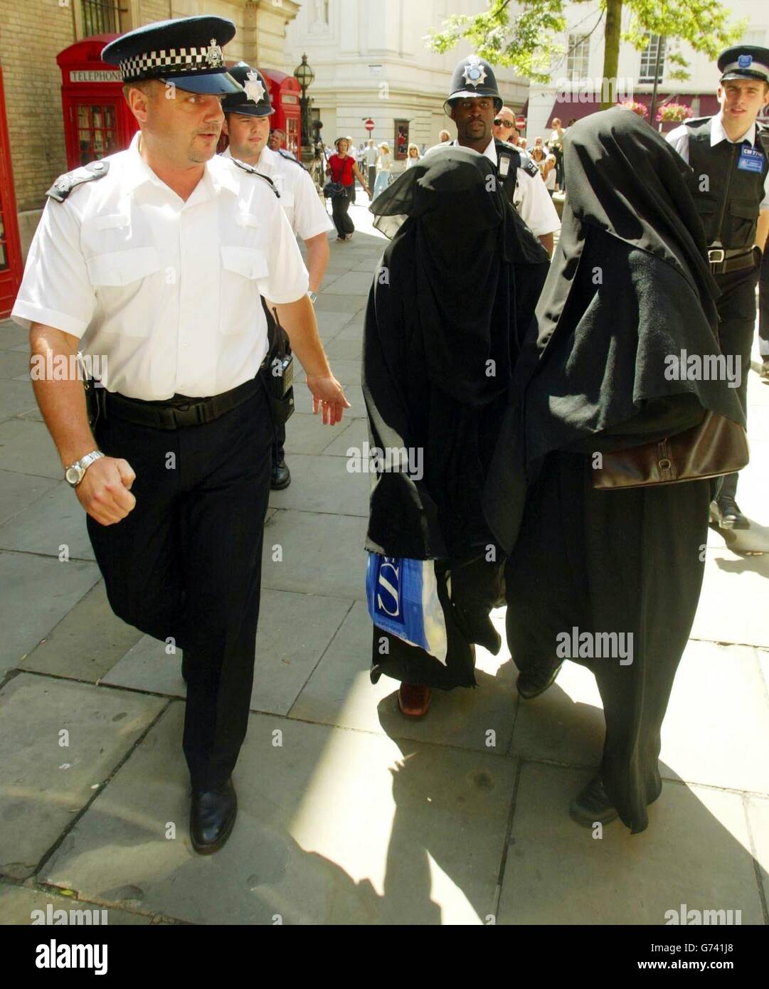 Family members are escorted by police officers as they leave Bow Street Magistrates Court after Babar Ahmad, 30, of Fountain Road, Tooting, south London, appeared following his arrest Thursday on an extradition warrant issued on behalf of the USA. The women, who declined to identify themselves to journalists, were in court where it was alleged that in December last year Ahmad was found in possession of a document detailing a US naval battle group operating the Strait of Hormoz in the Gulf in April 2001. Stock Photo