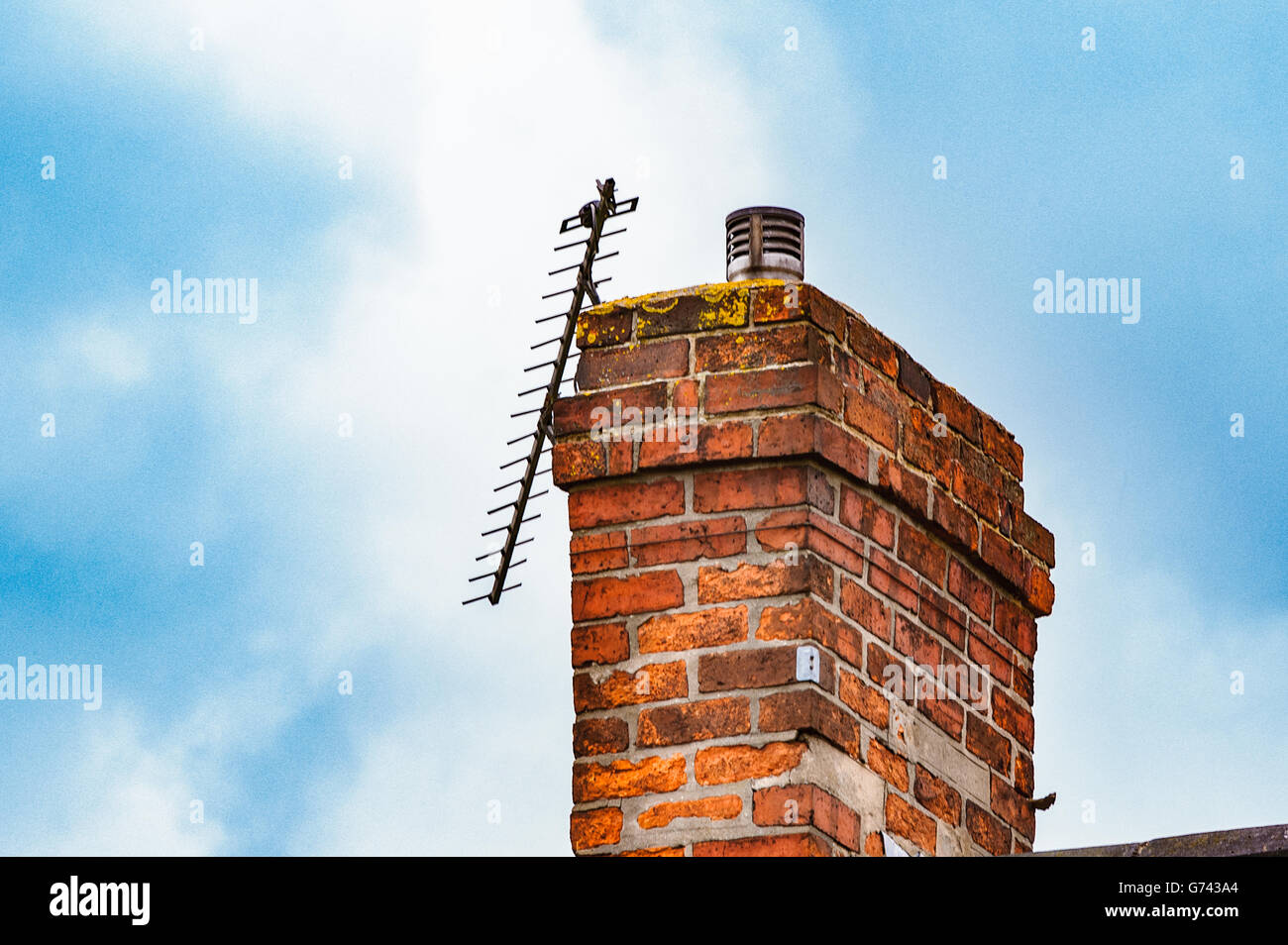 Broken TV aerial on a brick chimney against a blue sky Stock Photo