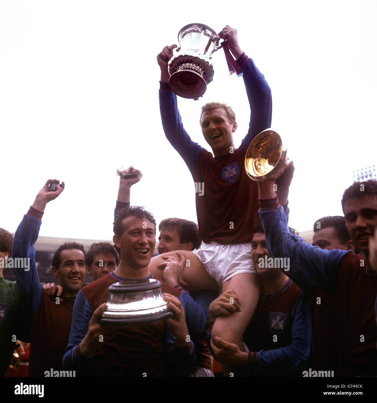West Ham United captain Bobby Moore lifts the FA Cup as his jubilant teammates chair him on their shoulders: (l-r) Eddie Bovington, Geoff Hurst, Ken Brown, John Bond, Moore, Peter Brabrook, Johnny Byrne, Ronnie Boyce Stock Photo