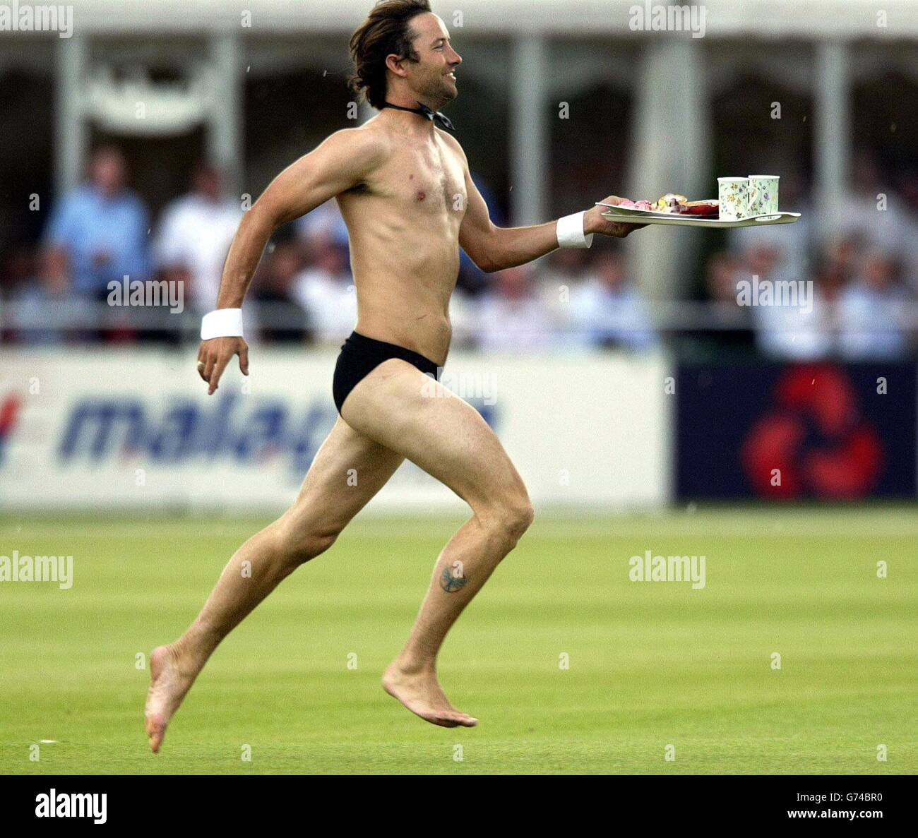 A streaker runs on the pitch holding a tea tray, during the first day of the third npower test against West Indies at Old Trafford, Manchester. Stock Photo