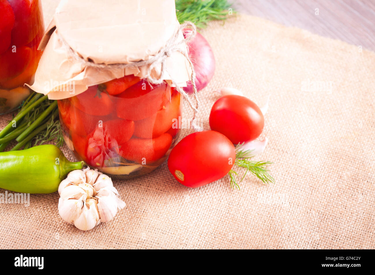 Canned tomatoes with garlic and herbs in a glass jar on the wooden