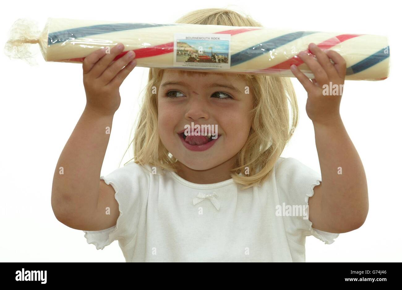 Two-year-old Jasmine Shaw licks her lips as she struggles under the weight of the 17 inch stick of rock that she is presenting to Queen Elizabeth II at her grandfather's shop on Bournemouth Pier in Dorset. The youngster will handover the seaside sweet when the Queen visits the resort. Stock Photo