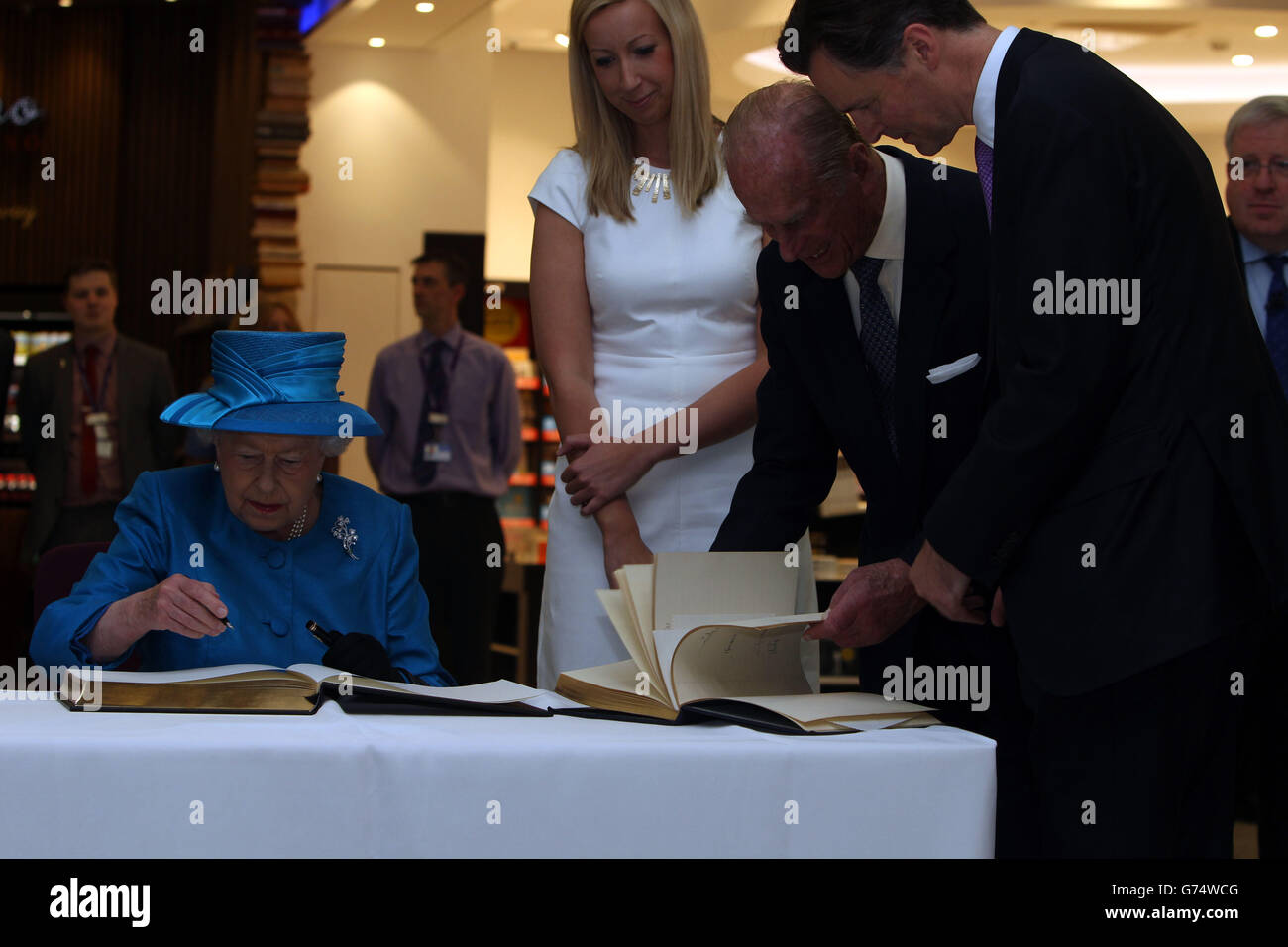 Queen Elizabeth II signs the new visitors book, as the Duke of Edinburgh looks through the visitors book from 1955, at the official opening of the new Terminal 2 The Queen's Terminal at Heathrow Airport. Stock Photo