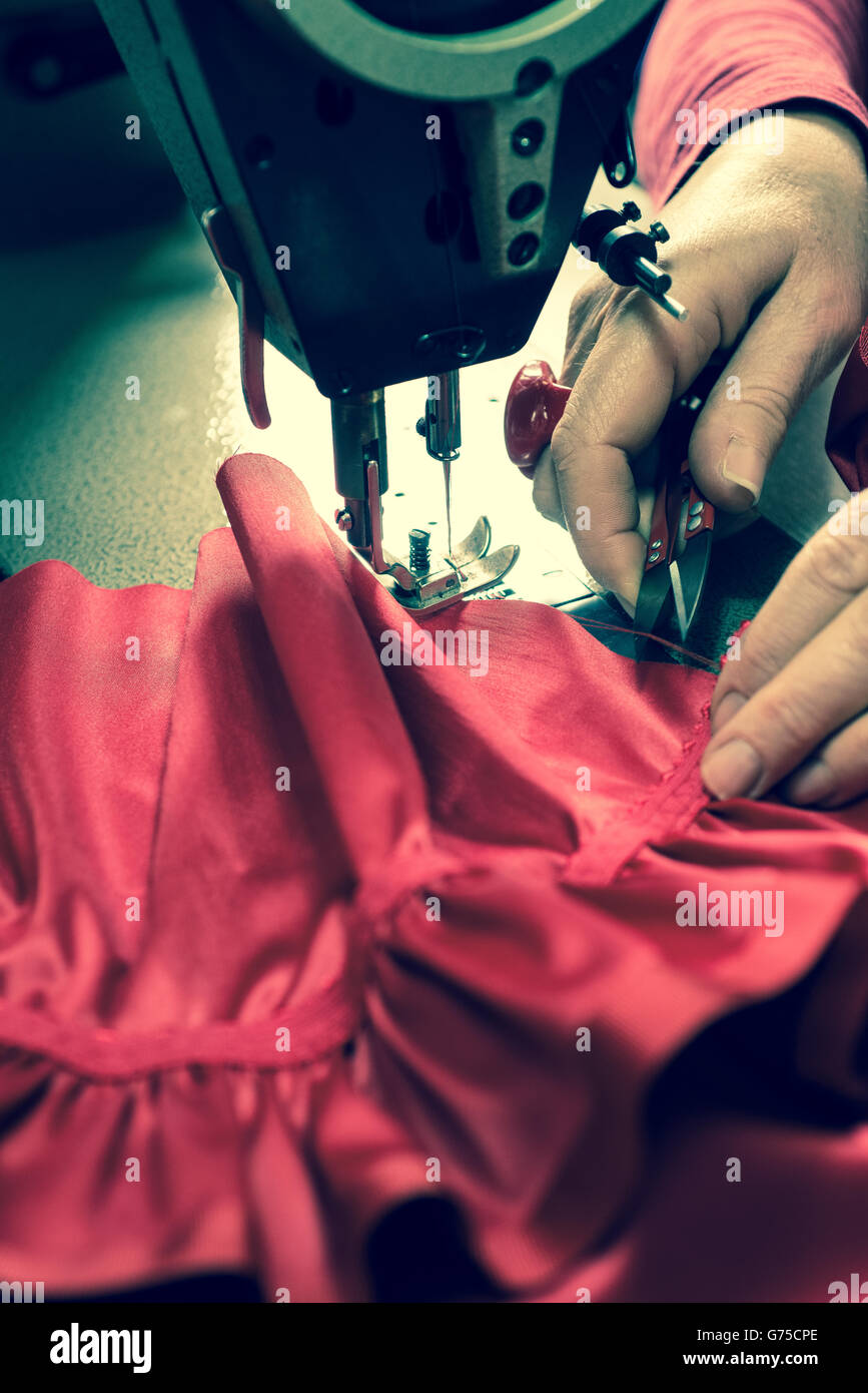 Tailor's hand about to trim excess thread from a sewn cloth on a sewing machine Stock Photo