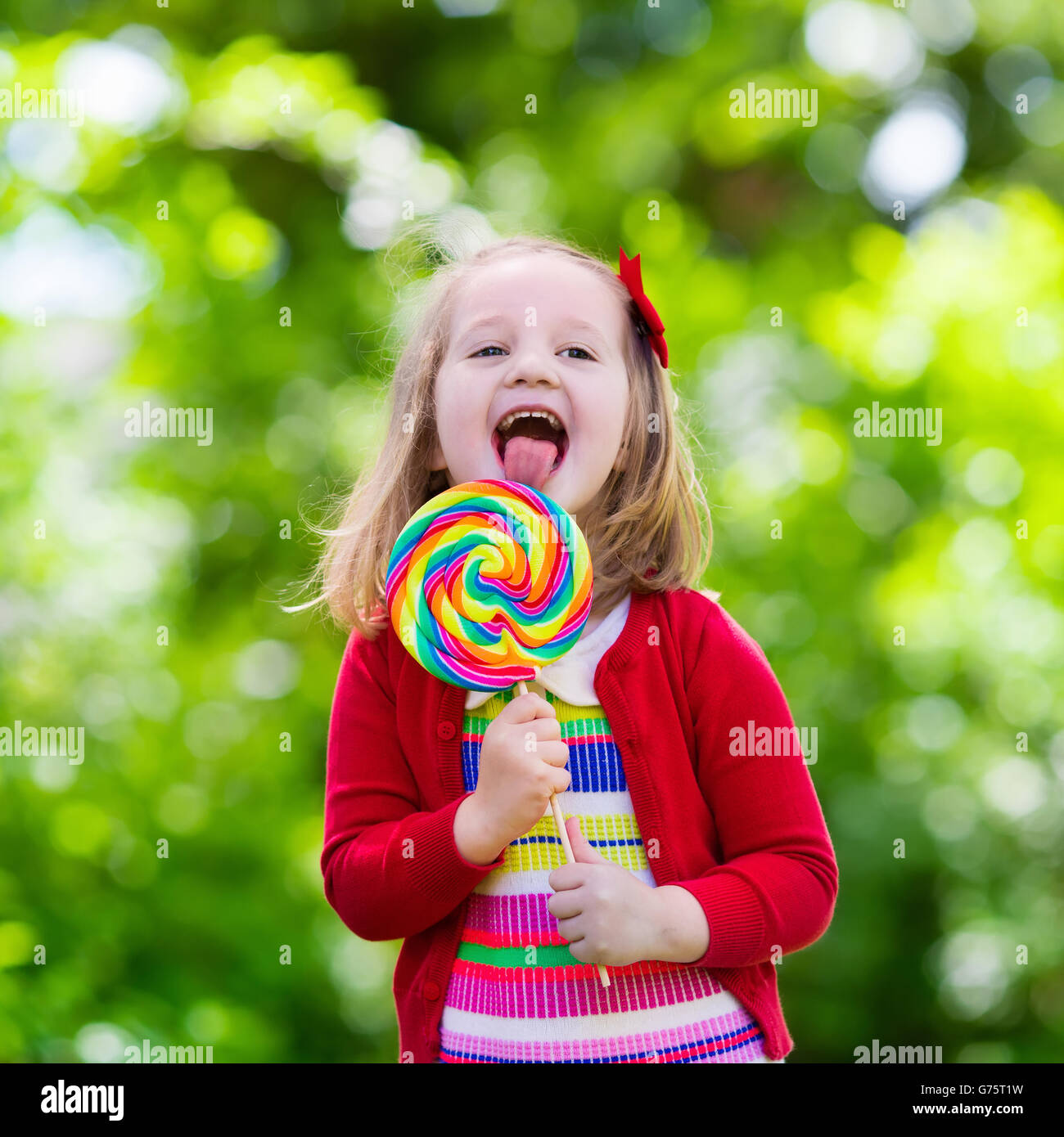 Cute little girl with big colorful lollipop. Child eating sweet candy bar. Sweets for young kids. Summer outdoor fun. Stock Photo