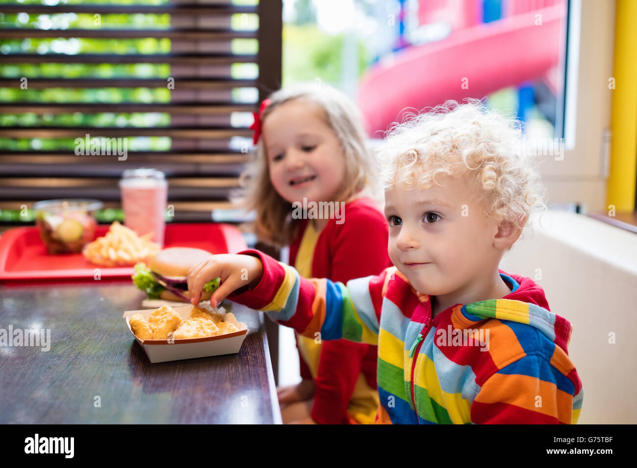 Little girl and boy eating chicken nuggets, hamburger and French fries in a fast food restaurant. Child with sandwich and potato Stock Photo