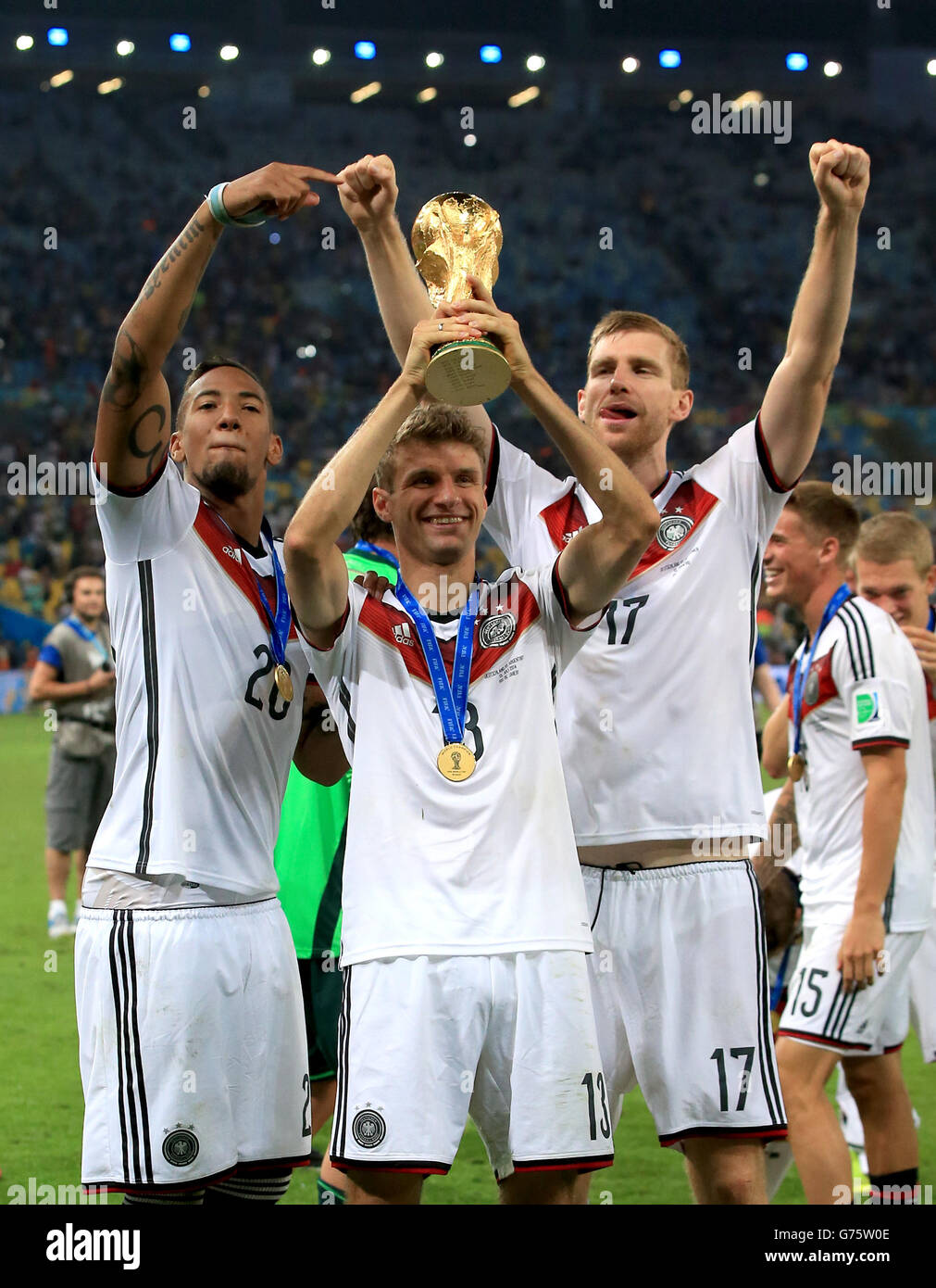 Germany's Thomas Muller celebrates on the pitch with the FIFA World Cup 2014 Trophy alongside teammates Per Mertesacker (right) and Jerome Boateng (left) Stock Photo