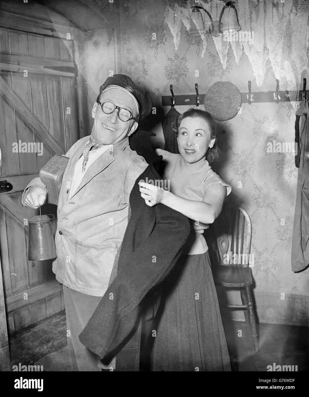 Diminutive Arthur Askey, an engine driver with a football complex in his latest comedy, is helped on with his regulation coat by his daughter, an co-actor Anthea Askey, during the dress rehearsal of 'The Love Match' at the Palace Theatre, London. Anthea is also his daughter in the play. Stock Photo