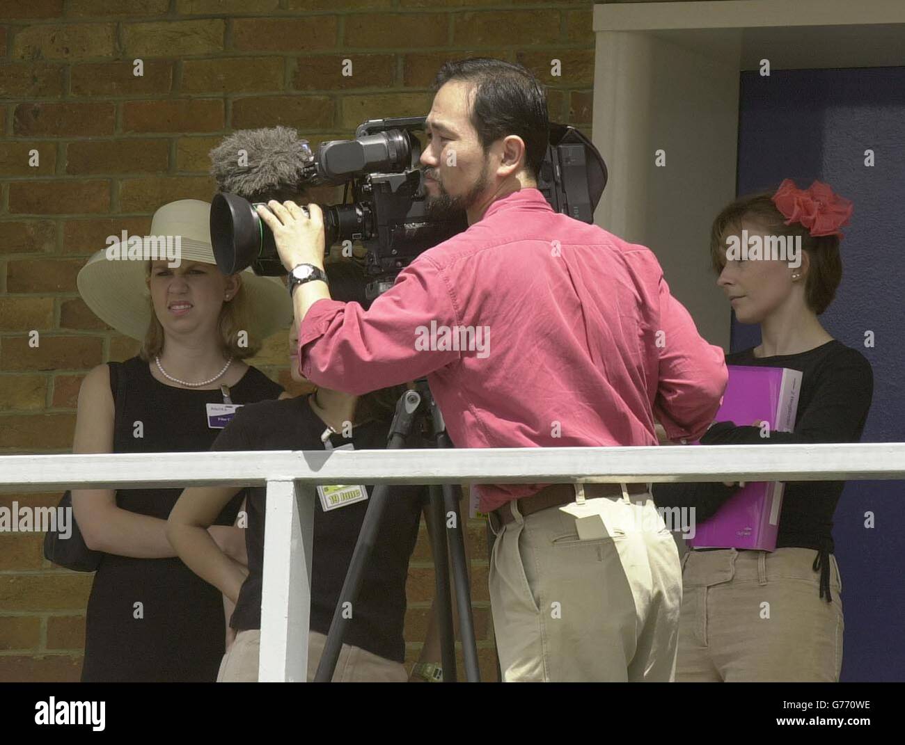A TV cameraman wears an open necked shirt with chinos, in the paddock area at Ascot race course