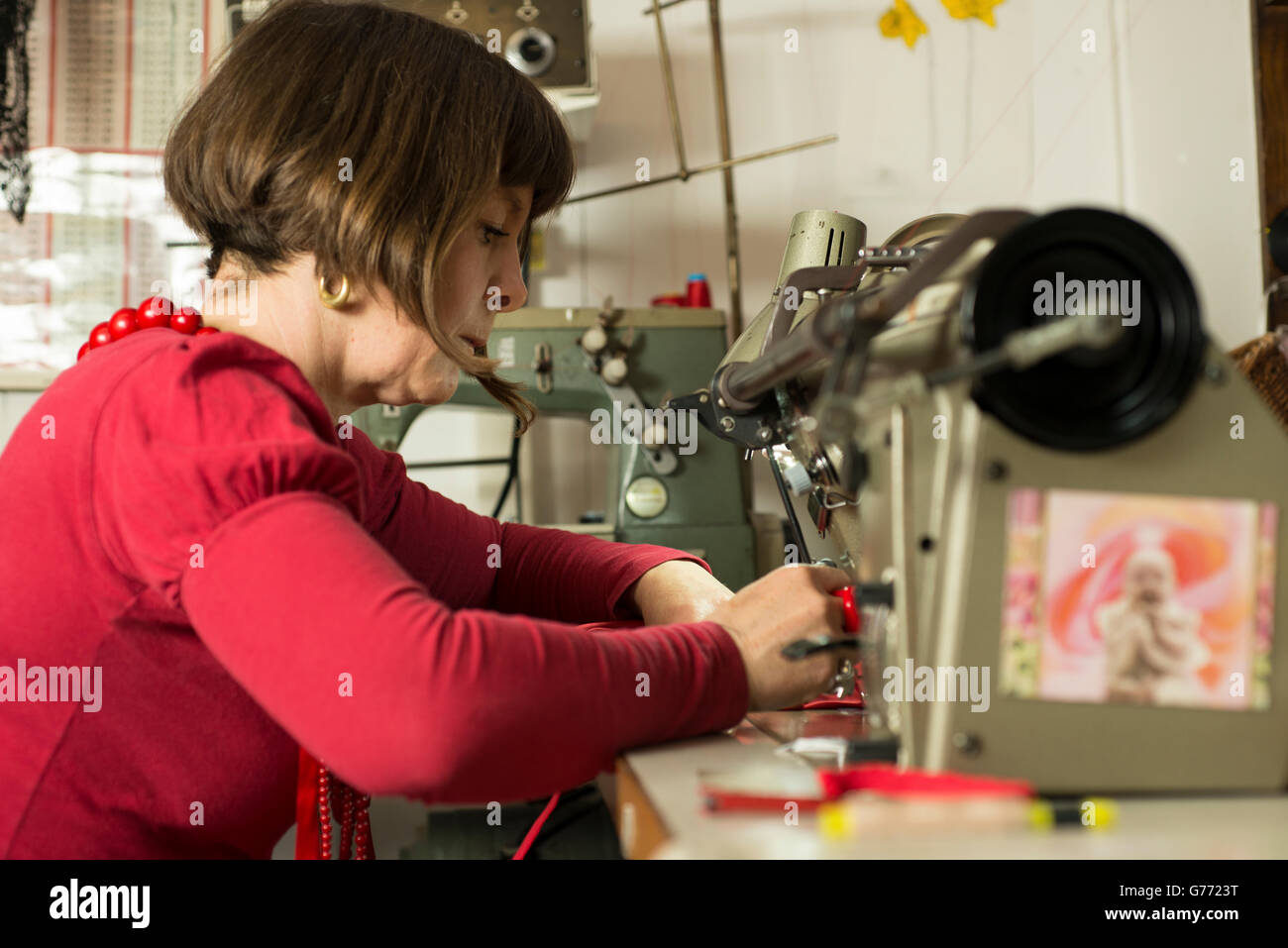 A dressmaker in red dress stitching fabric through a sewing machine Stock Photo