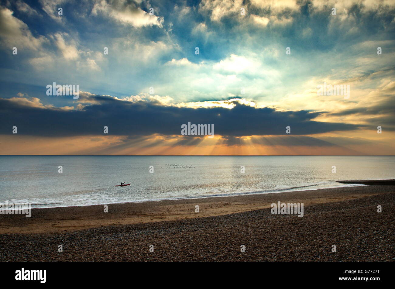 a lone Kayaker jn a seascape of Crepuscular rays breaking through some storm clouds Stock Photo