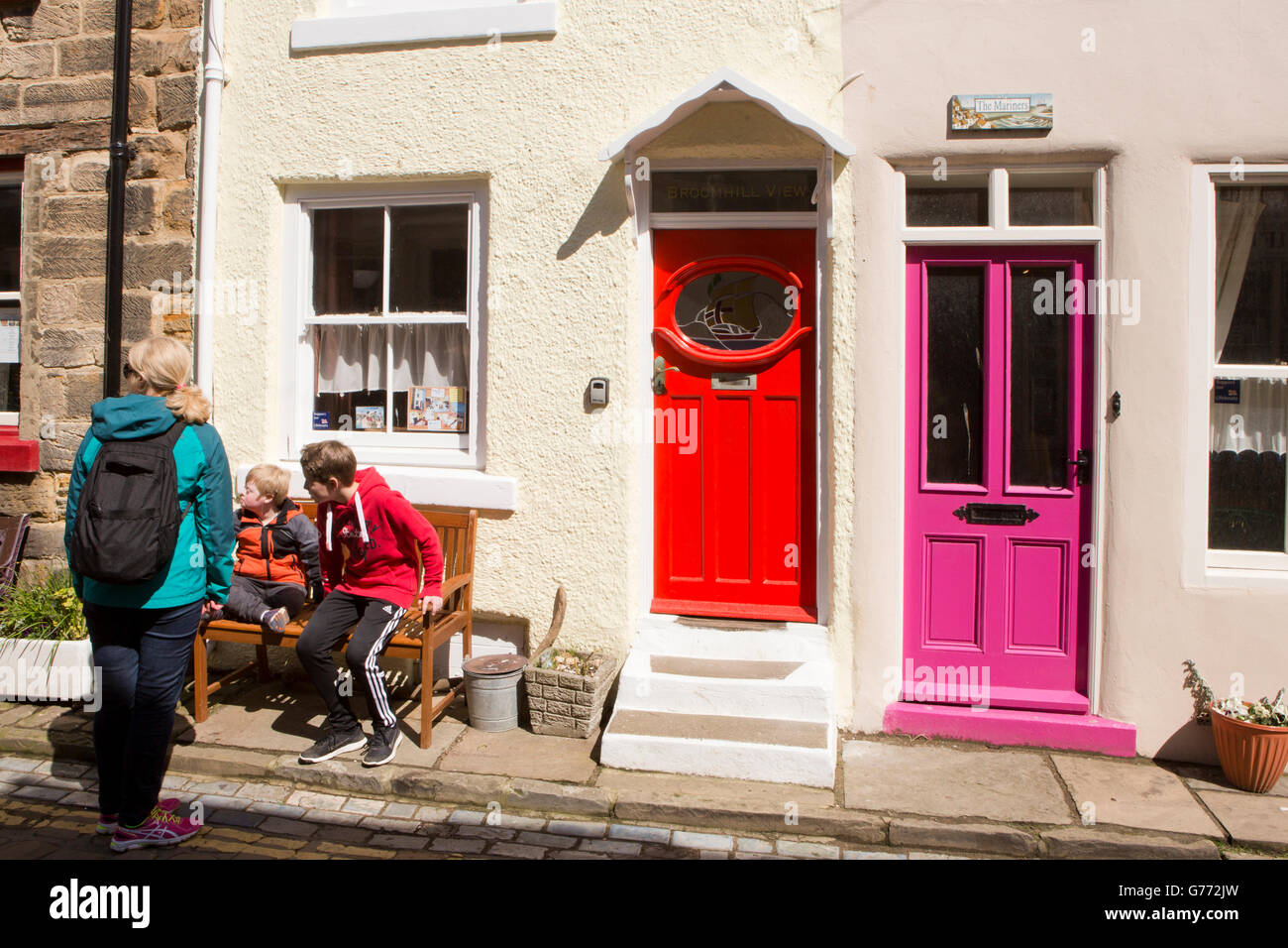 UK, England, Yorkshire, Staithes, High Street, people on bench in sun by bright red and purple painted doors Stock Photo