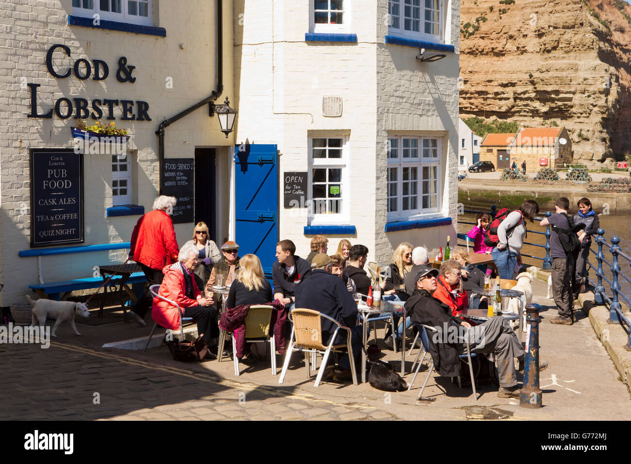 UK, England, Yorkshire, Staithes, High Street, customers sat at tables in sunshine outside Cod & Lobster pub Stock Photo