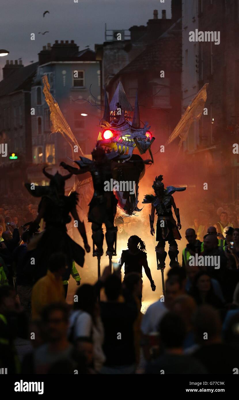 Acrobatic stilt-walkers, pyrotechnics, and giant moving dragons featuring the the sounds of a rock-opera score played by live musicians in a spectacle called 'Dragonus' as they make their way through the Streets of Galway as part of the Galway International Arts Festival. Stock Photo
