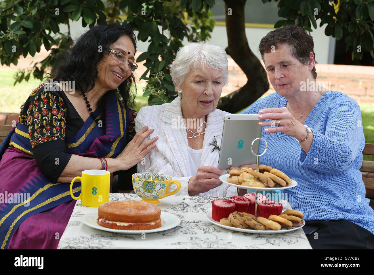 Actress June Whitfield (centre) and pensioners Chitra Banarjee (left) and Patricia Mary Sim enjoy tea and texts to launch the EE National Techy Tea Party Day, at Age UK in East London. Stock Photo