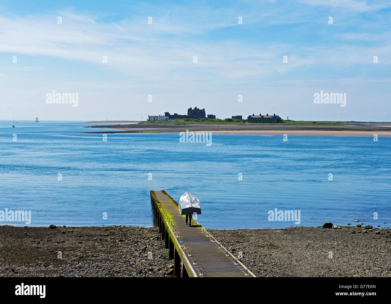 Man carrying dinghy along pier on Roa Island (with Piel Island in the distance), Cumbria, England UK Stock Photo